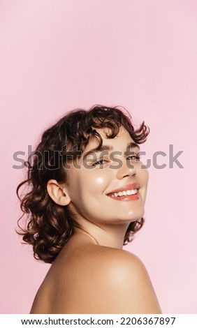 Skin care. Woman with beauty face and healthy facial skin portrait. Beautiful curly girl model with natural makeup touching glowing hydrated skin on pink background closeup. High quality image. Royalty-Free Stock Photo #2206367897