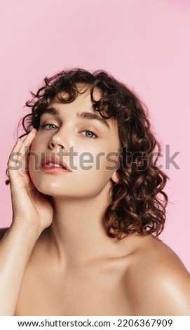 Skin care. Woman with beauty face and healthy facial skin portrait. Beautiful curly girl model with natural makeup touching glowing hydrated skin on pink background closeup. High quality image. Royalty-Free Stock Photo #2206367909