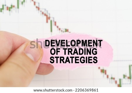 Business and trading concept. Against the background of the quote chart, a man holds a sign with the inscription - development of trading strategies