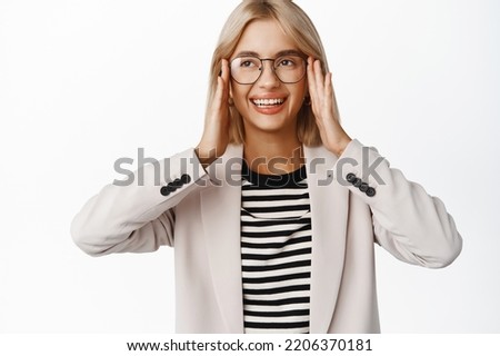 Portrait of smiling beautiful blond girl trying new glasses, picking eyewear, standing over white background.