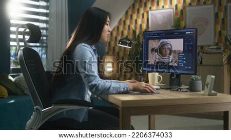 Female asian freelancer editing picture with astronaut on computer in photoshop while working remotely from home office
