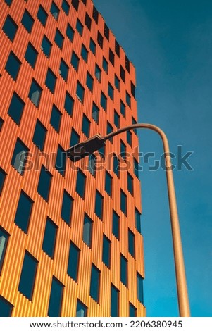 Modern office building exterior with glass facade on clear sky background. Transparent glass wall of office building with orange decoration with lantern. Creative Photo Element of facade of modern