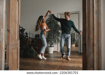 Full length of carefree young couple dancing at home together