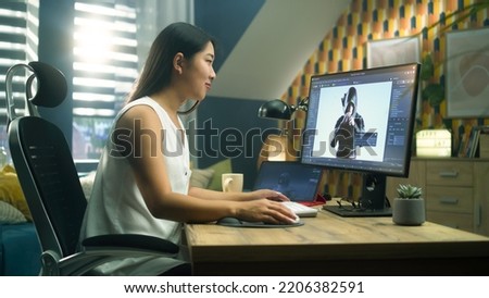 Asian woman creating 3D model of video game character in professional program using computer and digital tablet while working at home office