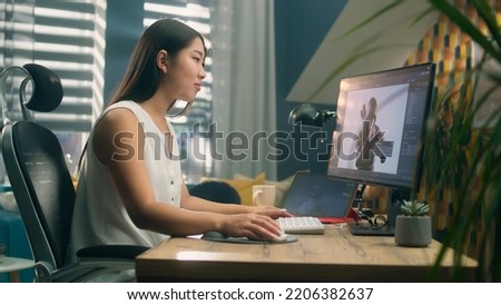 Asian woman creating 3D model of video game character in professional program using computer and digital tablet while working at home office