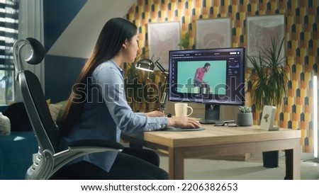 Asian woman editing photo in photoshop for customer on personal computer while sitting at the table at home office and working remotely