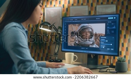 Female asian freelancer editing picture with astronaut on computer in photoshop while working remotely from home office