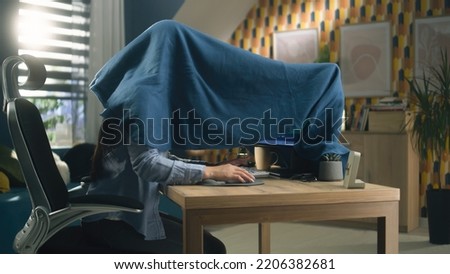 Woman sitting on chair at the table at home and doing color correction and grading, hiding under the blanket from sunlight rays of sun which comes from window Royalty-Free Stock Photo #2206382681