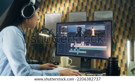 Concentrated asian woman sitting at the table and editing video for client in professional software using modern computer while working at home