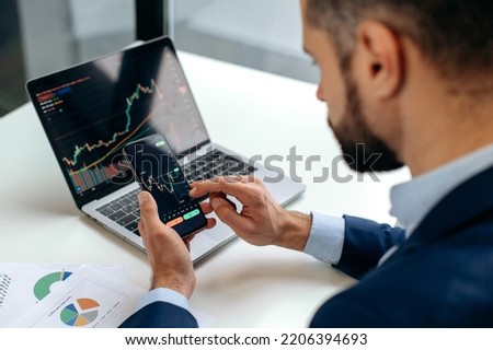 Close-up of laptop and smart phone screen with stock diagrams.Caucasian crypto trader investor using cellphone and laptop for cryptocurrency financial market analysis, buying or selling cryptocurrency Royalty-Free Stock Photo #2206394693