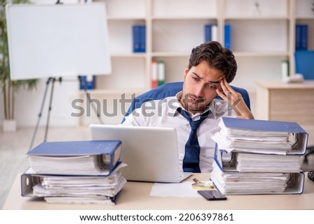 Young male employee and too much work in the office Royalty-Free Stock Photo #2206397861