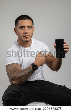 holding and showing a cell phone a young man with short hair a casual white t-shirt, technology and electronic device in studio, lifestyle