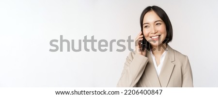 Smiling corporate woman in suit, talking on mobile phone, having a business call on smartphone, standing over white background