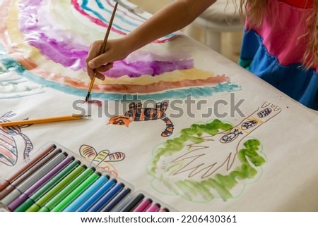 Laughing blonde curly barefoot little girl drawing paper art picture multicolored chalks sitting floor near childish hovel. Relaxed female kid happy childhood preschool early development entertainment Royalty-Free Stock Photo #2206430361