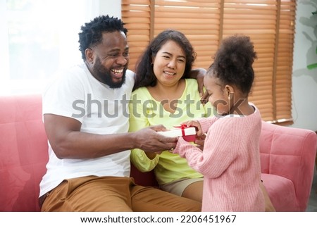 little girl giving gift box or present to mom and dad on sofa