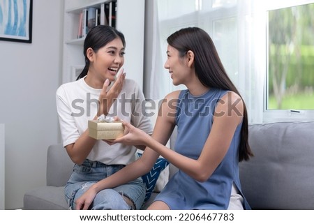 Asian lesbian woman congratulates her girlfriend on birthday, LGBT woman makes surprise, gives to beloved woman gift box with present, family celebrating life events. LGBT couple lifestyle concept.