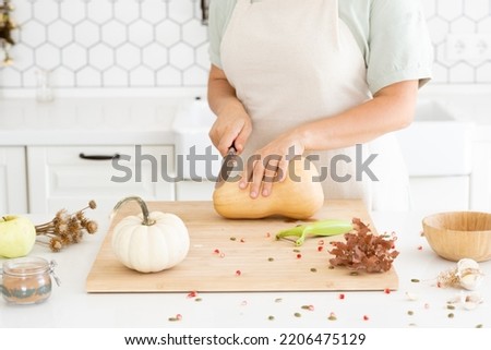 Woman hands cutting a butternut pumpkin in modern white kitchen. Making pumpkin soup at home. Autumn recipe. Food preparation. High quality photo