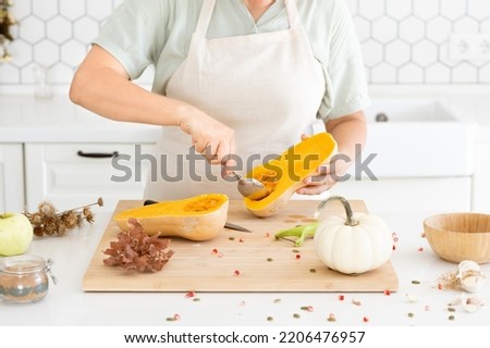 Woman hands scooping out the seeds of a butternut pumpkin in modern white kitchen. Cleaning process. Meal preparation.  Homemade autumn pumpkin soup recipe. High quality photo