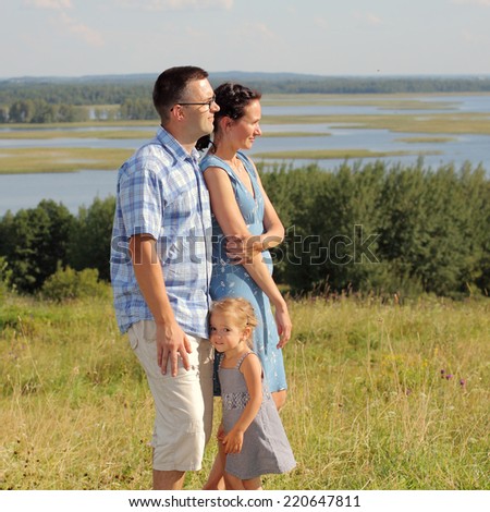 Happy family of three having fun on the hill in a landscape and open space. Outdoors on a background of sky and clouds.