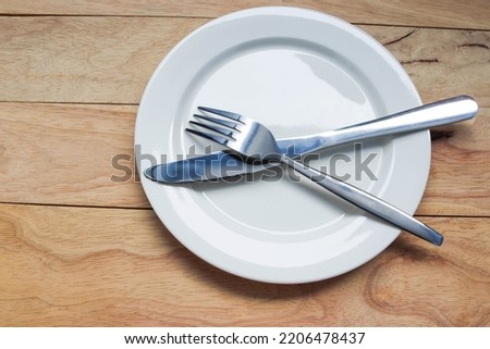Fork and, knife stainless steel on empty white plate, tableware isolated on wooden background closeup
