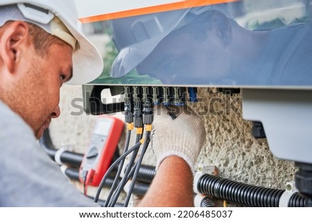 Man electrician installing solar panel system. Inspector in gloves making electrical wiring inverter and electric box. Concept of alternative and renewable energy. Royalty-Free Stock Photo #2206485037