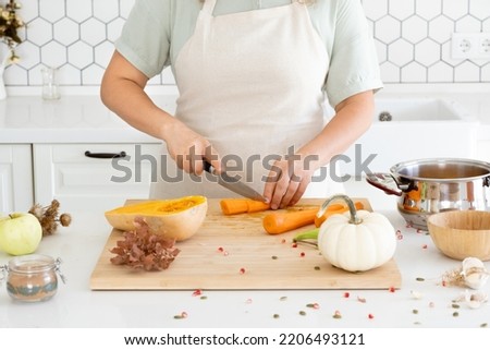 A woman cutting a carrot to prepare a tasty pumpkin soup for family. Meal preparation. Food picture. Holidays and cosy evening with family