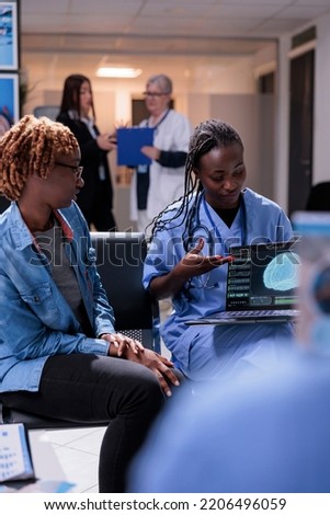 Nurse and patient analyzing brain scan on laptop, talking about tomography diagnosis and neural system on computer. Young woman and medical assistant doing checkup consultation in waiting room lobby.