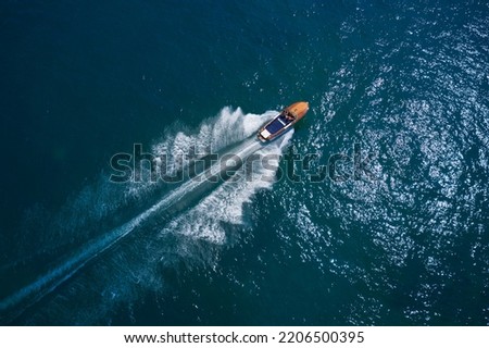 Classic Italian wooden boat fast moving aerial view. Luxurious wooden boat fast movement on dark water. Luxurious wooden motor boat rushes through the waves of the blue Sea. Royalty-Free Stock Photo #2206500395