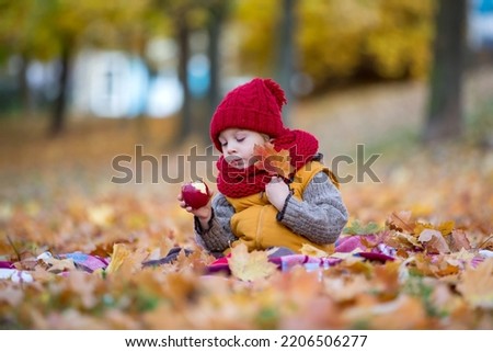 Happy child, playing with in autumn park on a sunny day, foliage and leaves all around him, eating apple