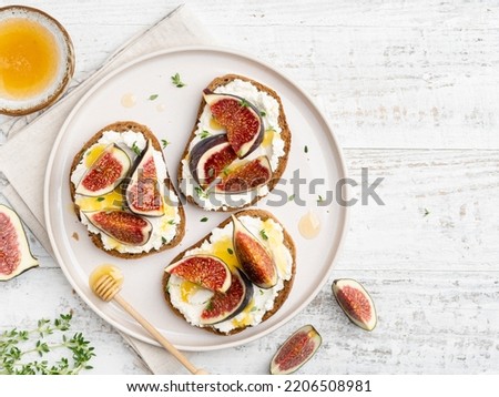 Ricotta, figs and honey bruschetta. Open sandwiches (toasts) with cream cheese, fresh sliced figs, syrup and thyme leaves. Tasty morning breakfast, lunch or dessert. Healthy eating concept. Top view. Royalty-Free Stock Photo #2206508981