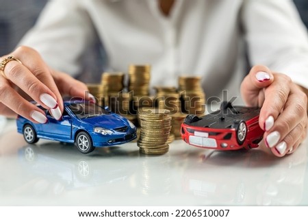 Hands of a woman holding two car models simulating an accident near a mountain of coins. Car insurance. Car accident driving safety