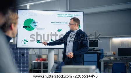 Male Engineer Points at Big Screen With Presentation and Talks About Green Energy and Solar Panels Future Possibilities. Engineering and Sustainable Energy Education Concept. Royalty-Free Stock Photo #2206514495