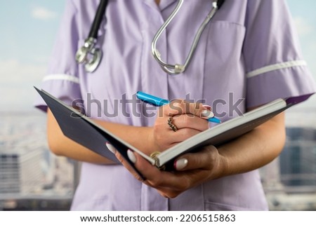 close-up photo of a nurse in uniform holding a journal and taking notes in a hospital. concept of medicine and health