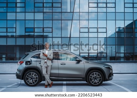 Businessman holding smartphone while charging car at electric vehicle charging station, closeup. Royalty-Free Stock Photo #2206523443