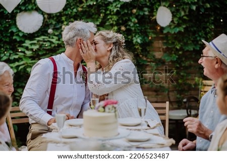 Mature bride and groom kissing at wedding reception with their family, outside in the backyard. Royalty-Free Stock Photo #2206523487
