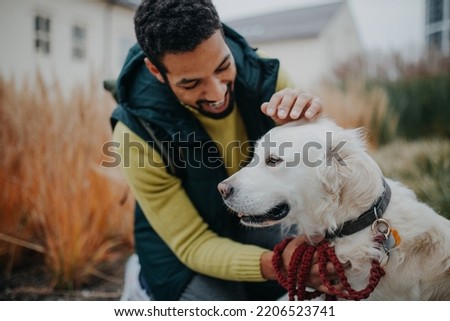 Happy young man stroking his dog outdoors in city park, during cold autumn day. Royalty-Free Stock Photo #2206523741