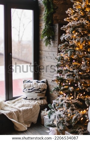 Atmospheric Christmas interior. Inspiration for home decor. Living room with large window. Holiday mood. Decorated Christmas tree. Cozy winter picture. Pillow and blanket on the windowsill 