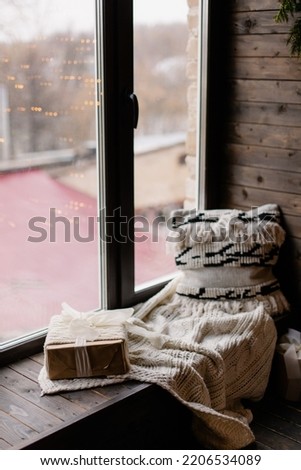 Atmospheric Christmas interior. Inspiration for home decor. Living room with large window. Holiday mood. Decorated Christmas tree. Cozy winter picture. Pillow, blanket and present on the windowsill 