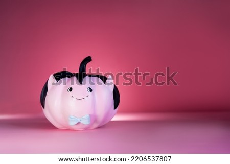 Halloween decorations on dark pink background. Funny and cute pink Vampire pumpkin with blue butterfly tie. Halloween card. Concept of entertainer, emcee for festive fall, autumn events. Copy space.
