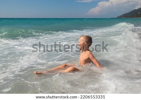 Excited little boy having fun at beach playing with waves. Caucasian kid enjoying summer holidays