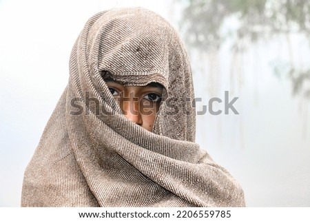 a homeless child is covering his body and face by a warm shawl in extreme cold weather  Royalty-Free Stock Photo #2206559785
