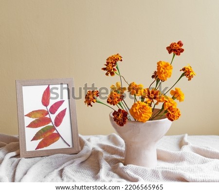 A vase with autumn flowers and a picture with autumn leaves on the table