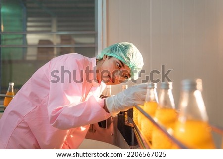 Woman Quality Control a fruit drink factory in glass bottles Inspecting glass bottle packaging for fruit juice drinks, Worker QC working in a drink water factory. Royalty-Free Stock Photo #2206567025
