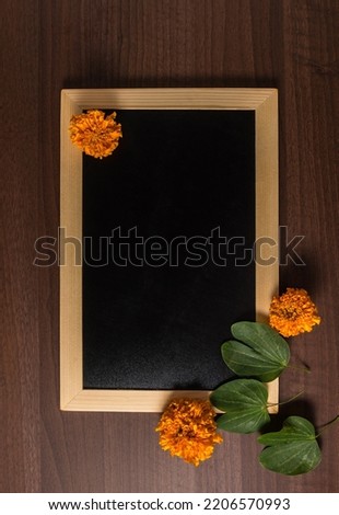 Photo of an empty, clean slate with wooden frame with Apte leaves and marigold flower. Dussehra festival template with blank space for the message. Royalty-Free Stock Photo #2206570993