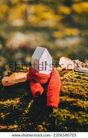 Miniature house in a red scarf on an autumn background with moss and yellow leaves. The concept of passive house heating. Thermal insulation of a building or dwelling. Energy crisis. Royalty-Free Stock Photo #2206580705