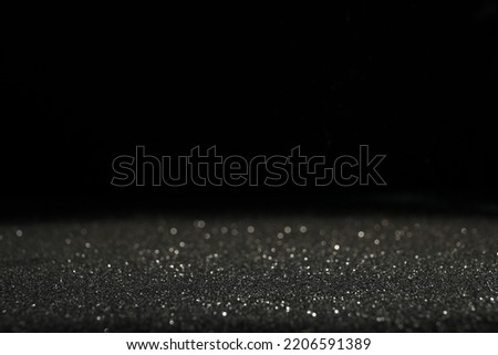 Shiny grey glitter on black background, space for text. Bokeh effect
