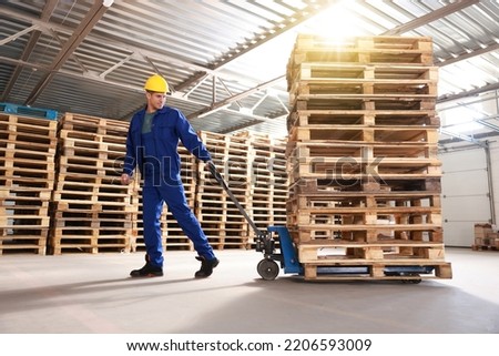 Worker moving wooden pallets with manual forklift in warehouse