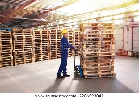 Worker moving wooden pallets with manual forklift in warehouse