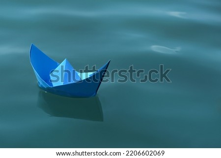Light blue paper boat floating on water surface, space for text