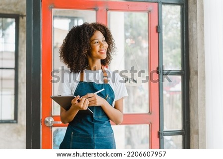 Happy young african american woman with apron standing at coffee shop door with open sign.